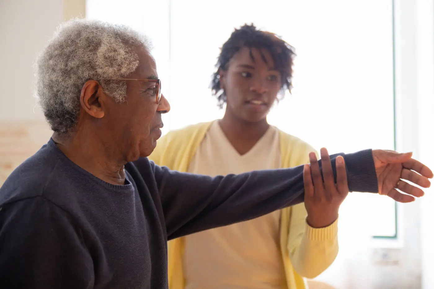 A caregiver helps an older man stretch his arm at home
