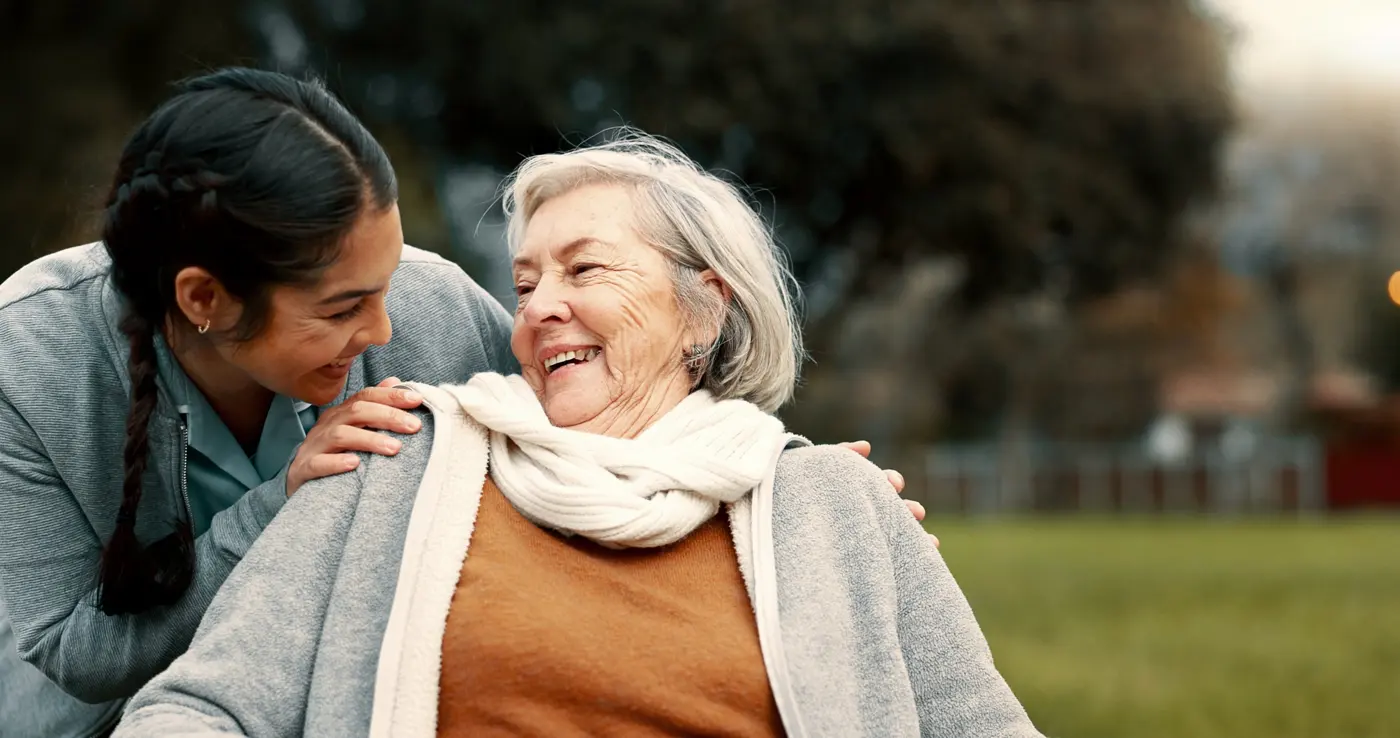 A caregiver and an older woman laughing outdoors