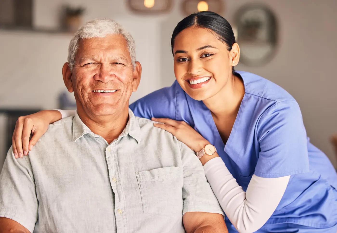 A smiling caregiver with her hands on an older man's shoulders